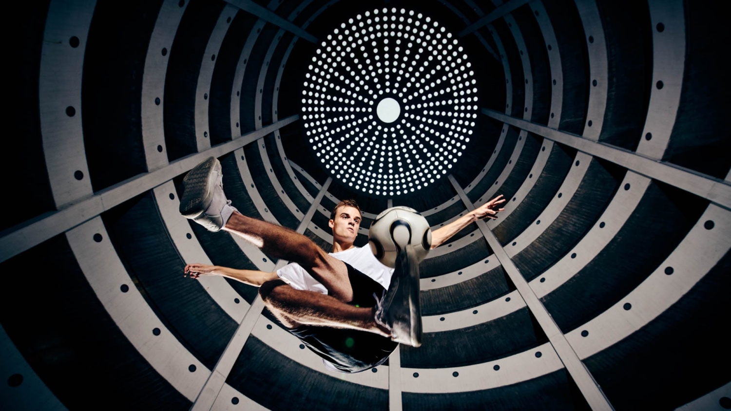 Jannis Gasser schwebt mit einem Fußball in einem modernen, kreisförmigen Gebäude mit geometrischen Lichtmustern.
