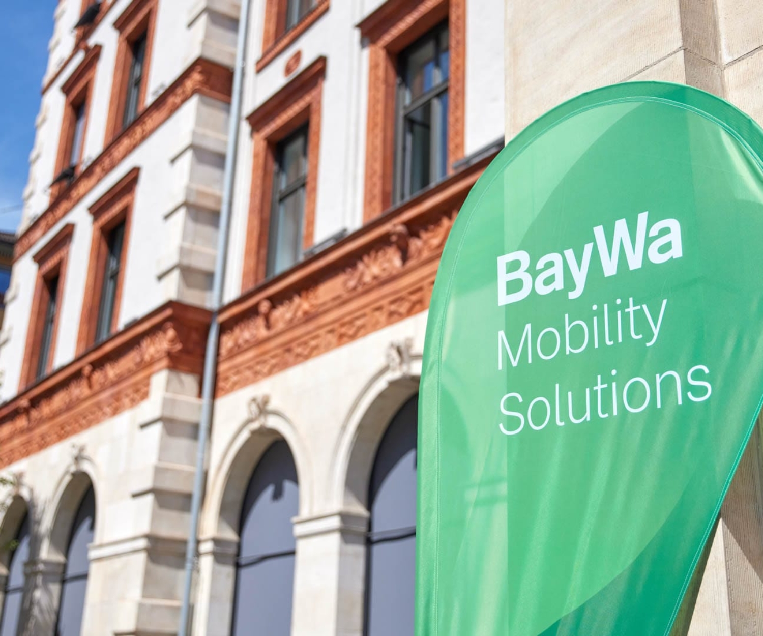 Grüner BayWa Mobility Solutions Banner vor dem Veranstaltungsgebäude der BayWa Charging Night 2024.