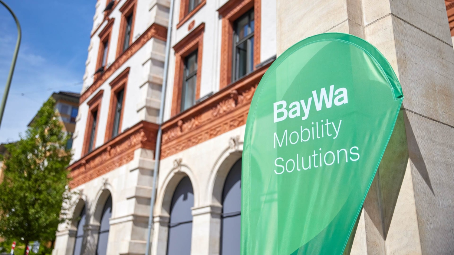 Grüner BayWa Mobility Solutions Banner vor dem Veranstaltungsgebäude der BayWa Charging Night 2024.