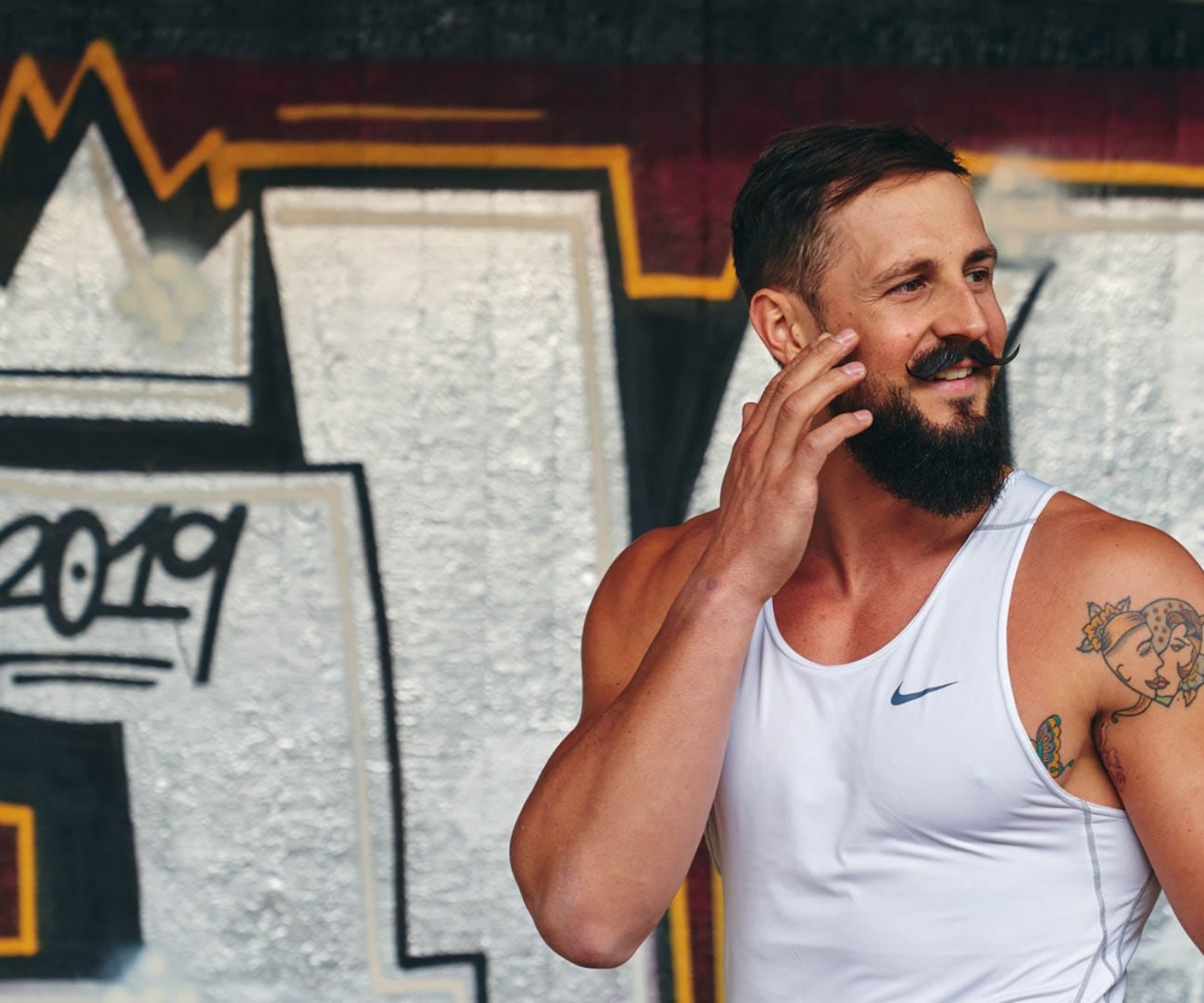 Simon Kunz lacht entspannt in Sportkleidung vor einer Graffiti-Wand, Fitness und Bodybuilding in München