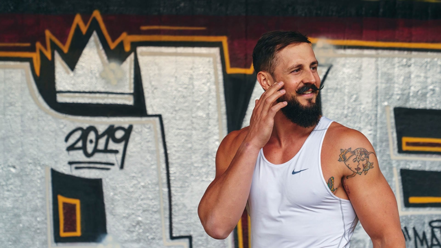 Simon Kunz lacht entspannt in Sportkleidung vor einer Graffiti-Wand, Fitness und Bodybuilding in München