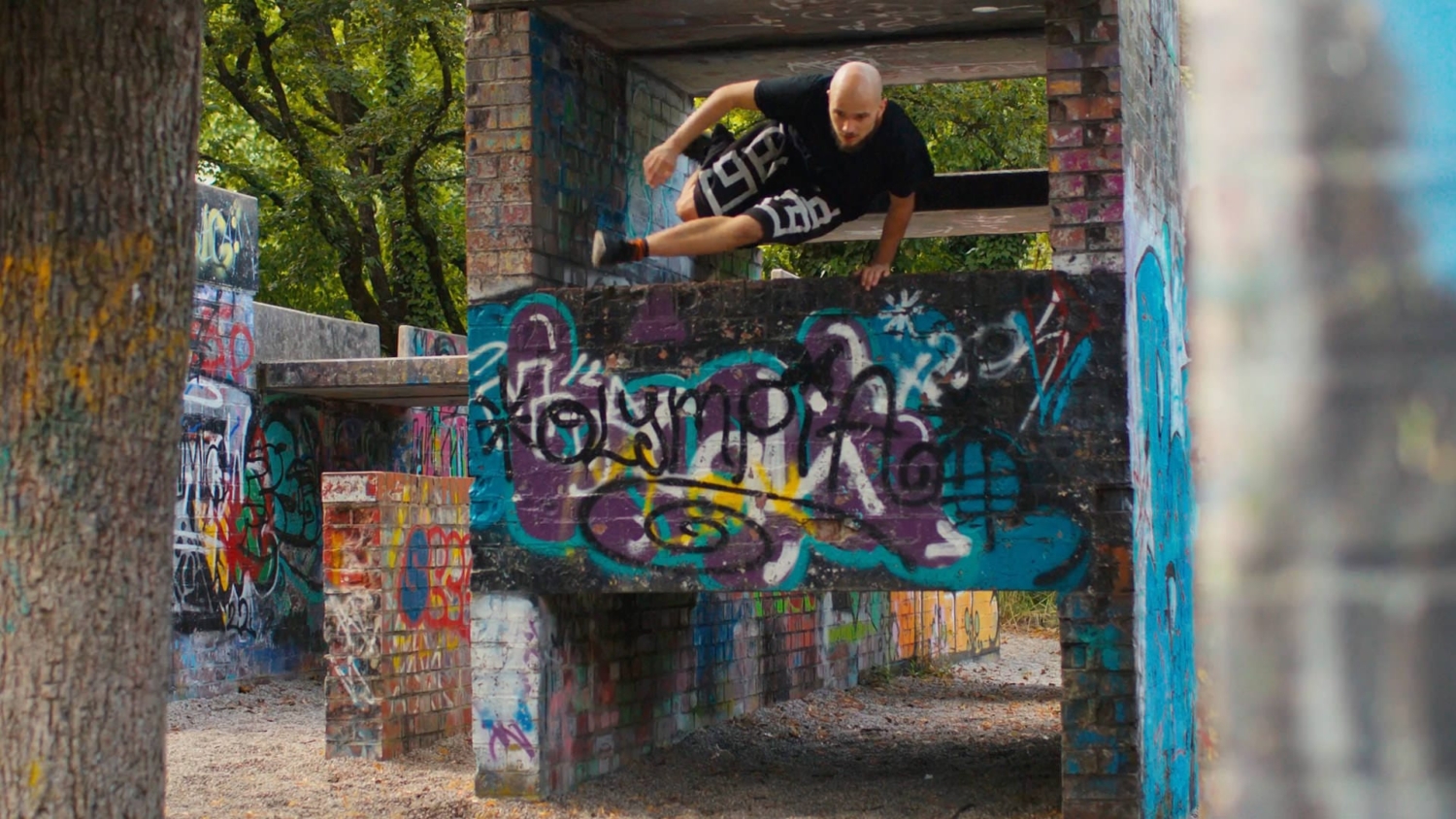 Athlet beim dynamischen Parkour-Sprung im Olympiapark München, umgeben von Graffiti und urbaner Architektur