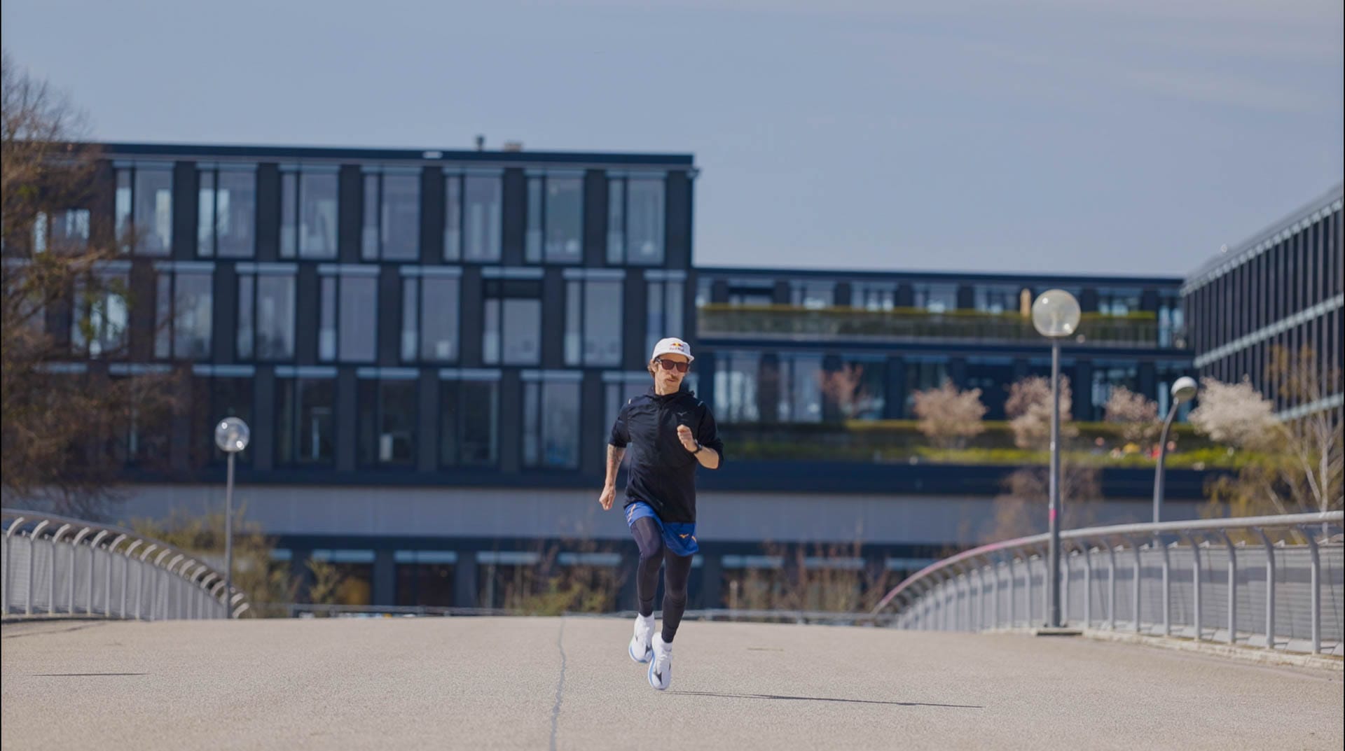 Ultraläufer Flo Neuschwander läuft auf einer Brücke im Olympiapark – frontal, im Sonnenlicht