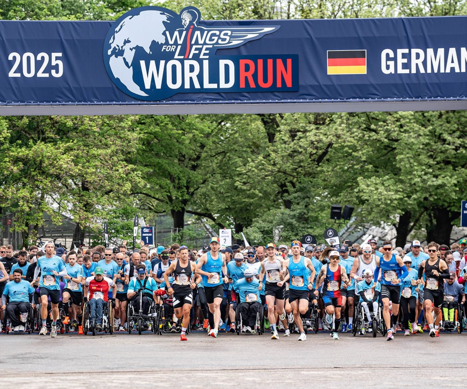 Der Start des Wings for Life World Run 2025 in München mit zahlreichen Läuferinnen und Läufern unter dem offiziellen Eventbanner