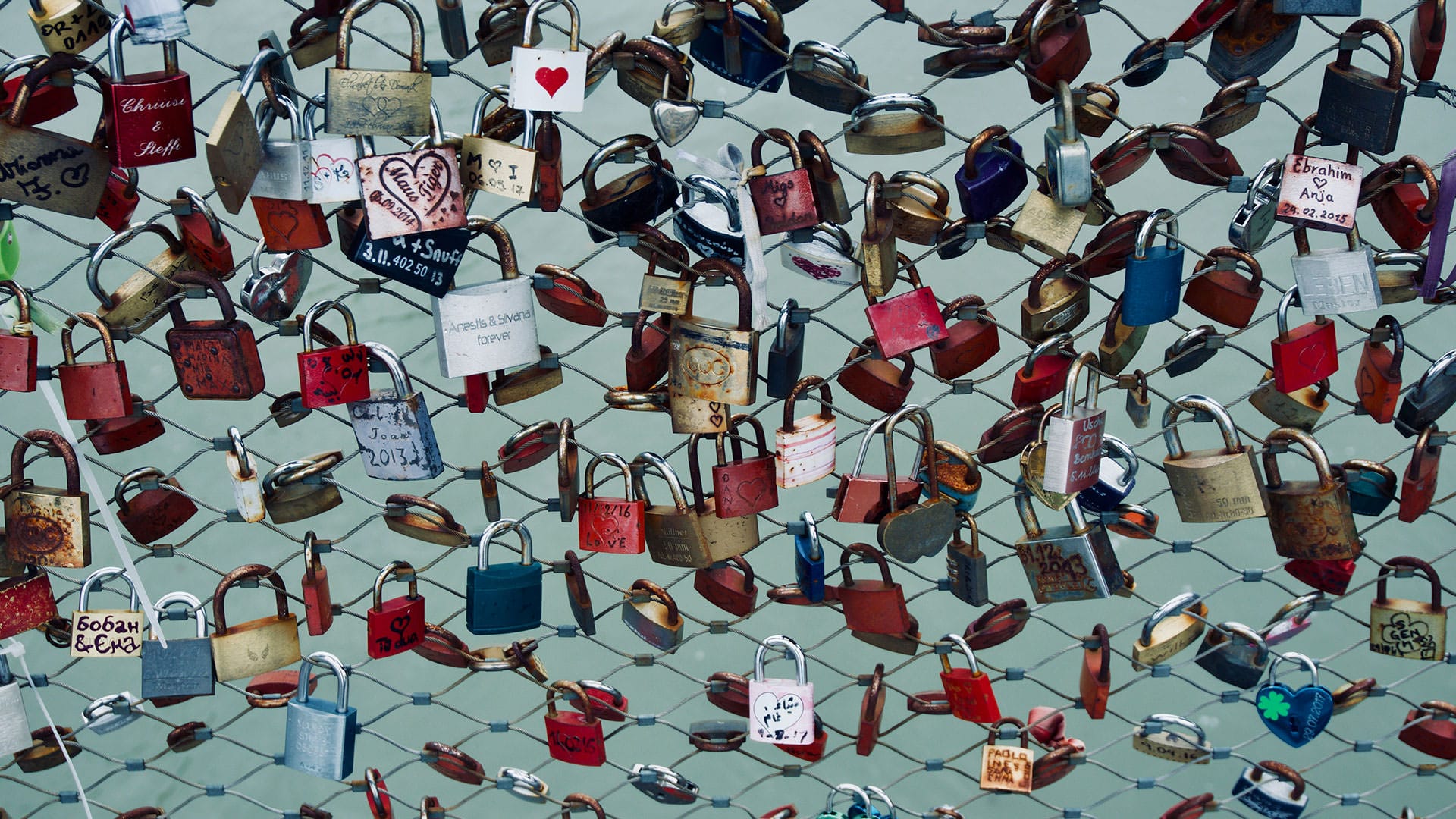 Zahlreiche bunte Liebesschlösser hängen an einem Zaun, Symbol für persönliche Geschichten und emotionale Verbundenheit.