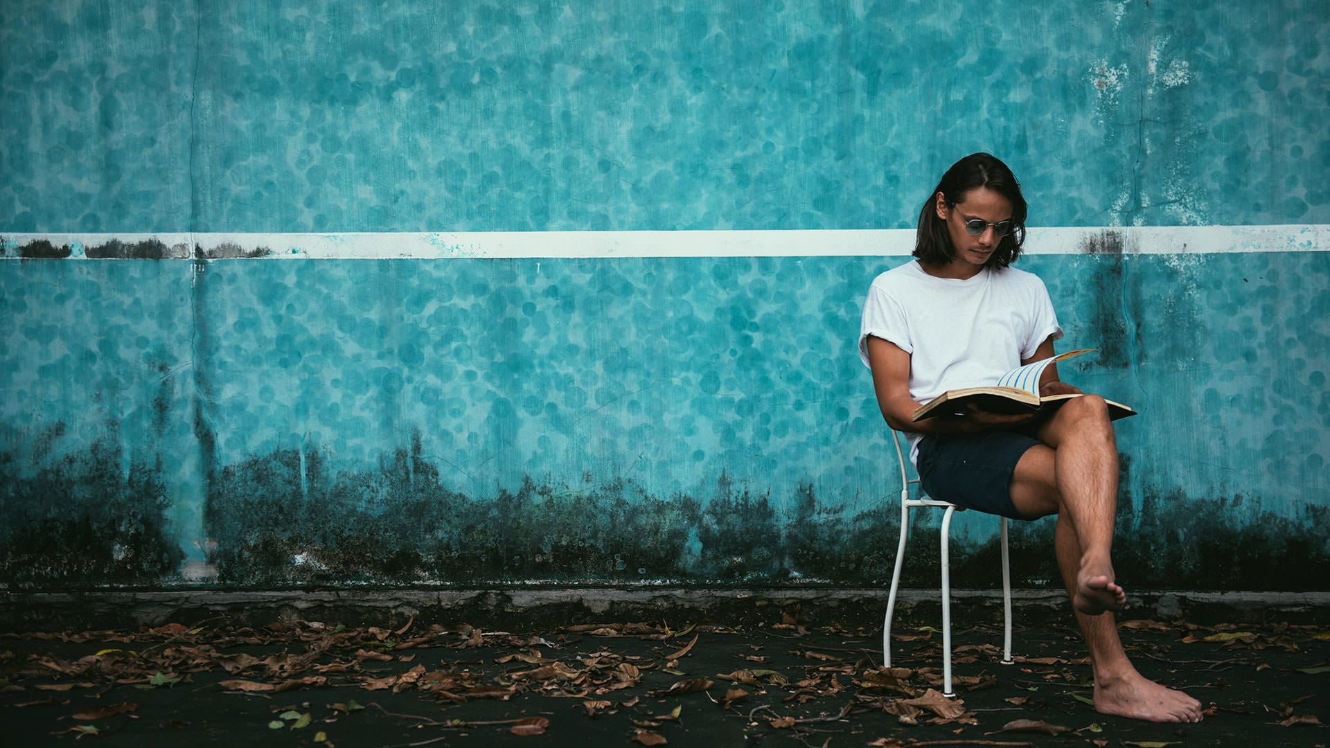Ein junger Mann liest barfuß vor einer blauen Wand in einem Buch – Symbol für Ruhe, Konzentration und den Kern einer guten Geschichte