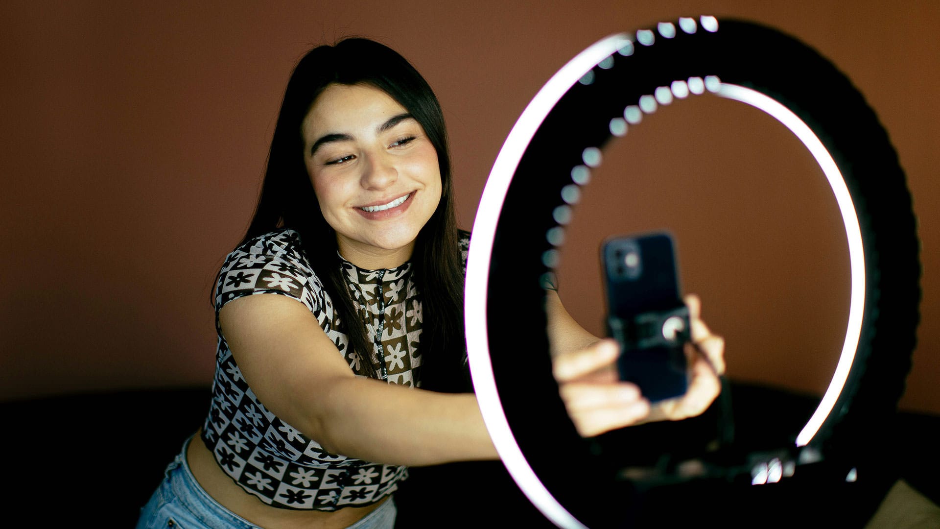 Junge Frau richtet Smartphone in Ringlicht aus für eine Aufnahme im Stil von User-Generated Content im Unternehmensvideo