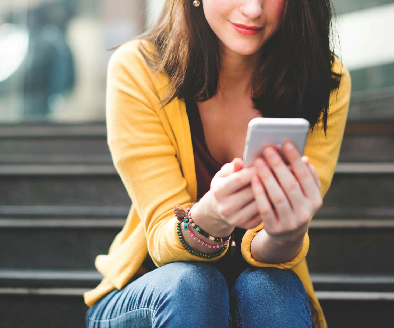 Junge Frau sitzt auf einer Treppe und schaut sich Kurzvideos für Unternehmen auf dem Smartphone an