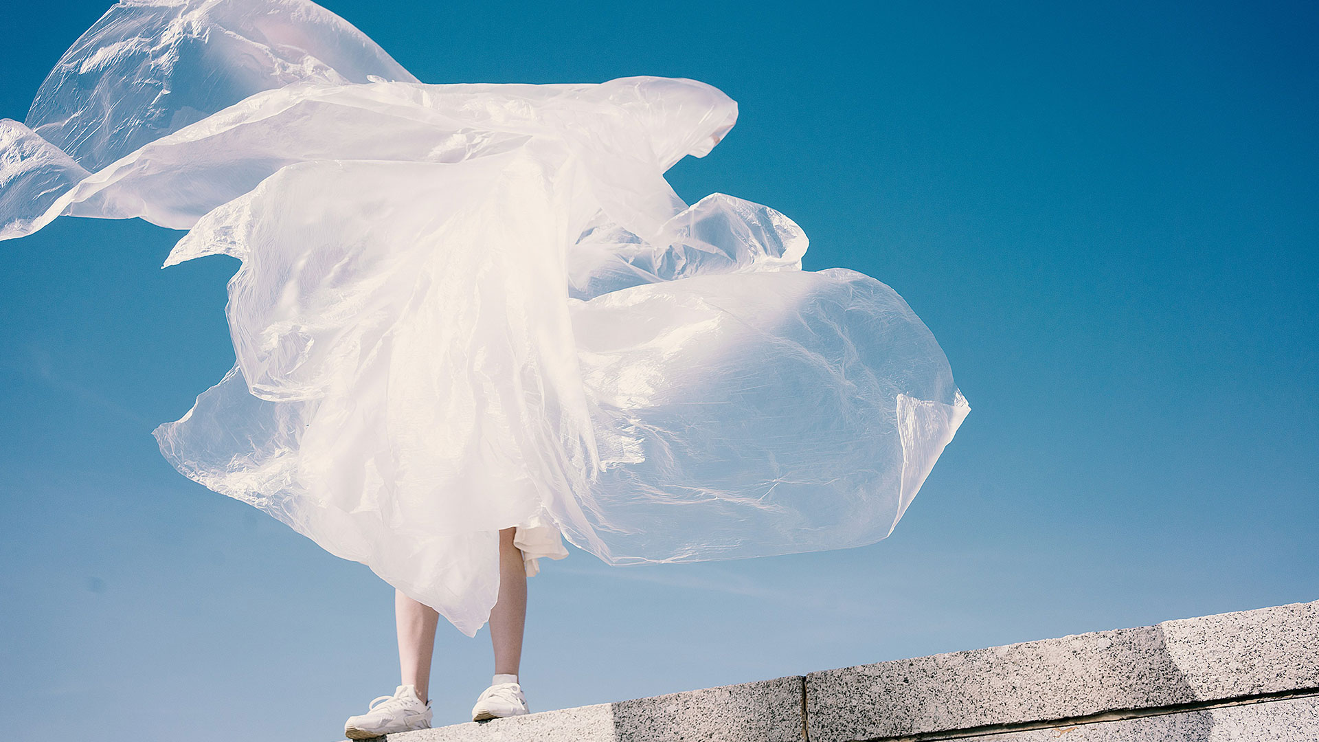 Eine Person mit wehender Plastikfolie im Wind vor blauem Himmel – Hinweis auf Ressourcenbewusstsein und Nachhaltigkeit in der Filmproduktion